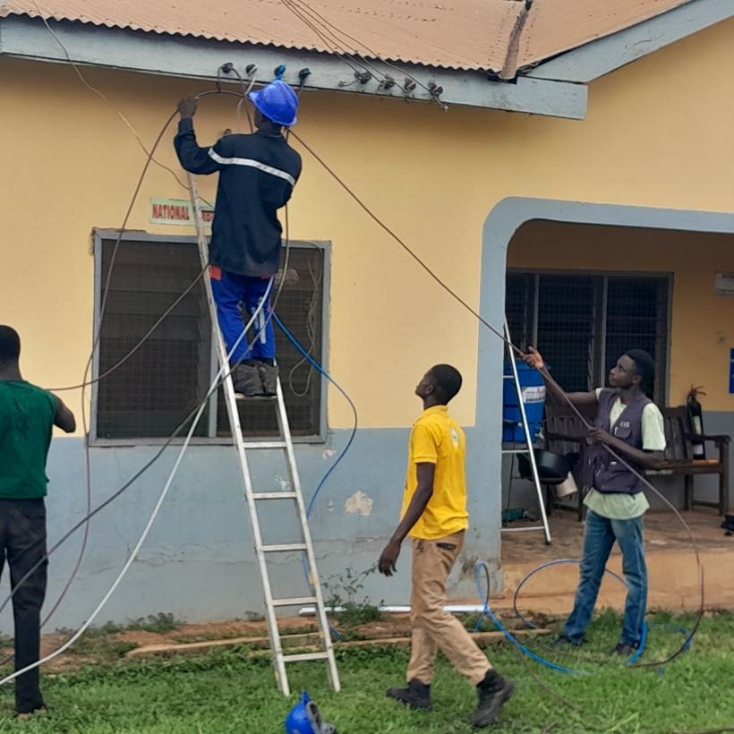 A student on a ladder running cable along a building